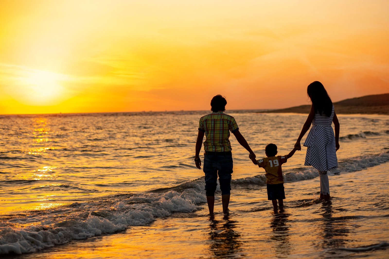 A family holding hands at the water's edge at sunset on a beach in Vietnam
